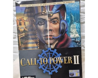 Può includere: Una scatola del videogioco "Call to Power II". La copertina presenta un'immagine divisa di un faraone e una figura futuristica, con il titolo del gioco in oro e un ingranaggio blu. Il logo Activision è in basso.