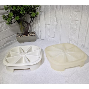 Puede incluir: Dos cubiteras de plástico blanco. Una es opaca, la otra translúcida. Cada cubitera tiene forma cuadrada con esquinas redondeadas y está dividida en ocho secciones triangulares. Las cubiteras están sobre una superficie blanca.