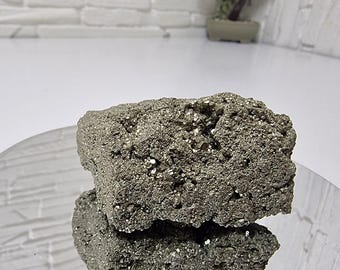 May include: A raw pyrite mineral specimen featuring a metallic, brassy-gold luster and a rough, crystalline surface texture. The cluster displays numerous small, cubic facets that catch the light, creating a reflective, textured appearance.