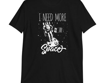 May include: Black t-shirt with a white astronaut standing on the moon with a flag. The text "I NEED MORE SPACEO" is printed on the shirt.
