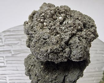 May include: A raw mineral specimen featuring a cluster of metallic, brass-colored pyrite crystals with a cubic structure. The formation has a rough, textured surface with a reflective sheen, showcasing a dense arrangement of small, sharp, geometric mineral cubes.