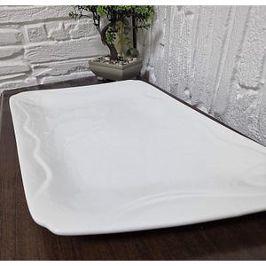 Puede incluir: Una fuente rectangular blanca con un dise&ntilde;o sutil veteado. Los bordes son ligeramente curvos y la superficie es lisa. La fuente es adecuada para servir aperitivos o postres. El tema general es la decoraci&oacute;n del hogar y los utensilios de cocina.
