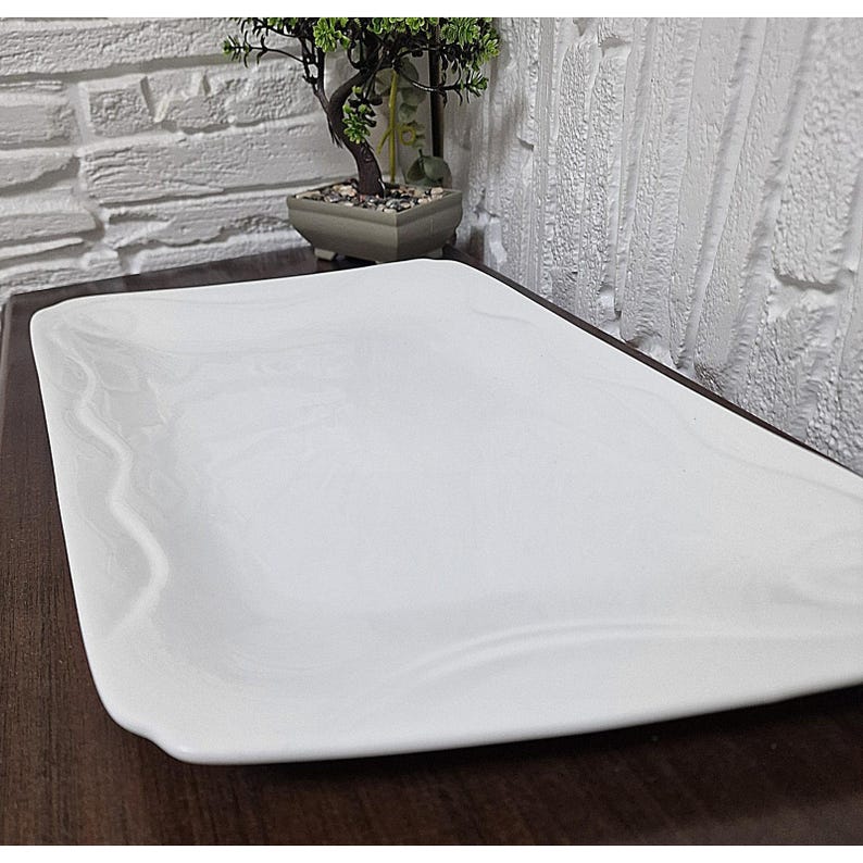 Puede incluir: Una fuente rectangular blanca con un dise&ntilde;o sutil veteado. Los bordes son ligeramente curvos y la superficie es lisa. La fuente es adecuada para servir aperitivos o postres. El tema general es la decoraci&oacute;n del hogar y los utensilios de cocina.