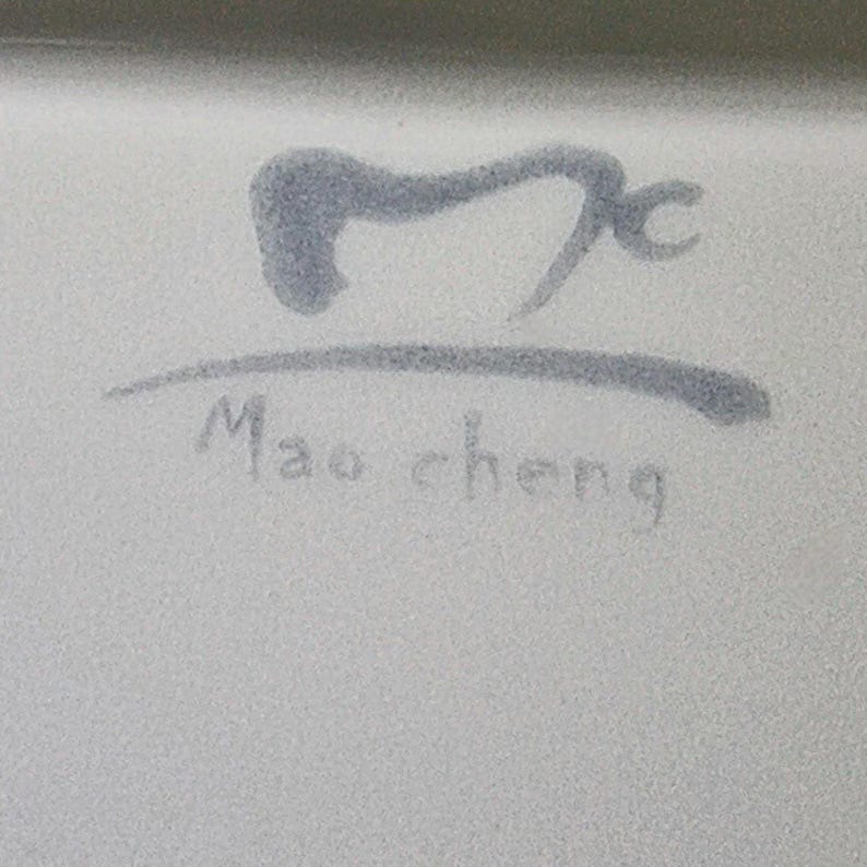 Puede incluir: Primer plano de una superficie blanca con un dise&ntilde;o gris estilizado y el texto "Mao cheng" en una fuente manuscrita. El dise&ntilde;o es un s&iacute;mbolo abstracto.