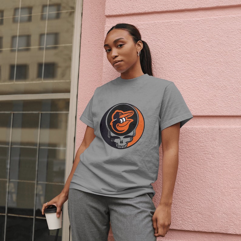 May include: A gray t-shirt with a black and orange graphic of a baseball mascot's head inside a skull. The mascot is wearing a baseball cap.