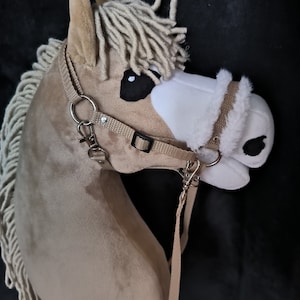 Può includere: Una testa di cavallo di peluche marrone e bianca con una briglia beige e una lunga criniera bianca. La testa di cavallo è un giocattolo per bambini.