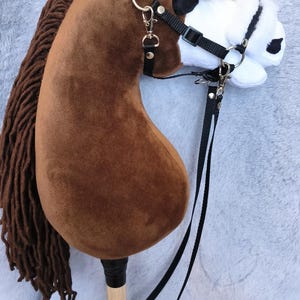 May include: A brown hobby horse with a black bridle and reins. The horse has a brown mane and a white and black face. The stick is made of wood. A fun toy for children.