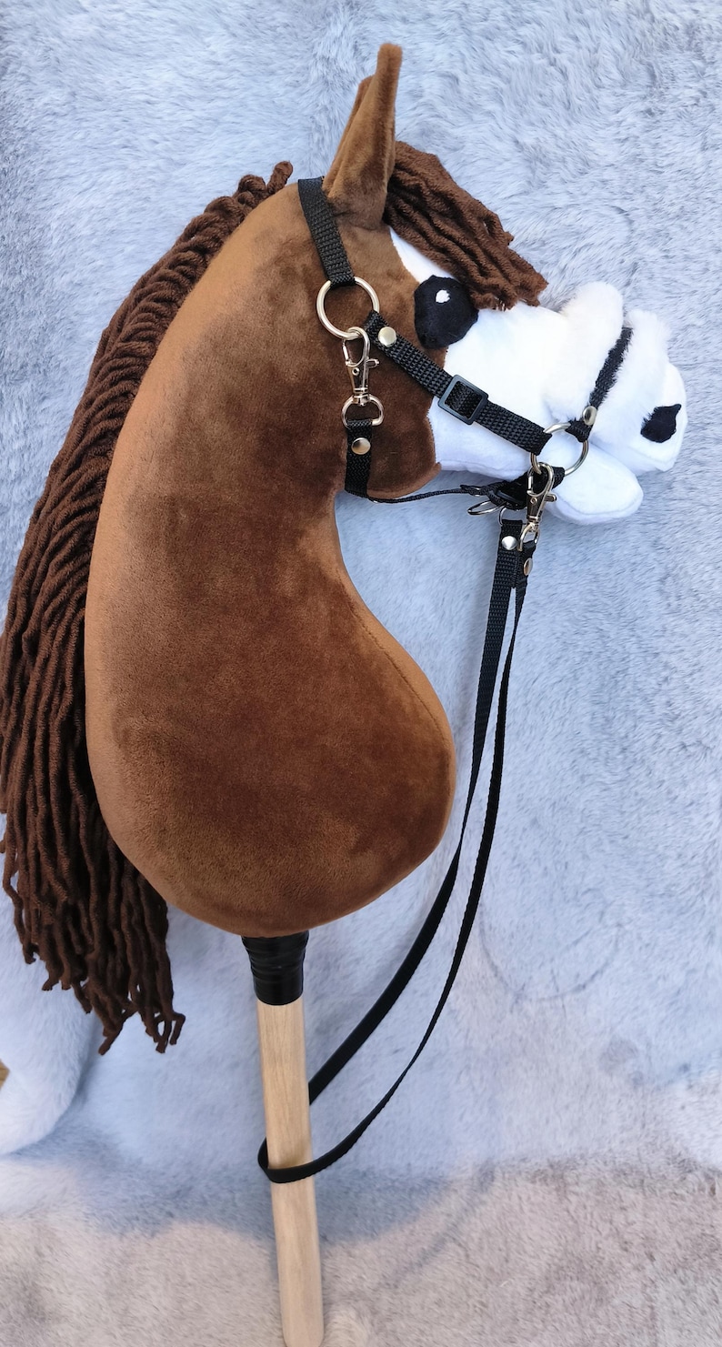 May include: A brown hobby horse with a black bridle and reins. The horse has a brown mane and a white and black face. The stick is made of wood. A fun toy for children.