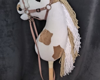 May include: A white and brown plush rocking horse with a long white mane and tail. The horse has a brown leather bridle with a metal buckle. The horse is attached to a wooden stick.