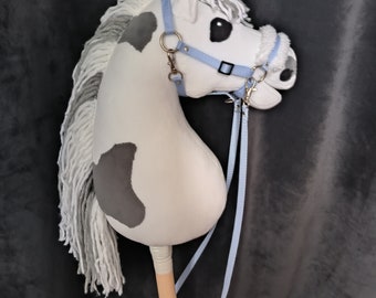 Puede incluir: Un caballo de balancín blanco y gris con una brida y riendas azules. El caballo tiene una larga melena y cola blancas. El caballo está en un palo de madera.