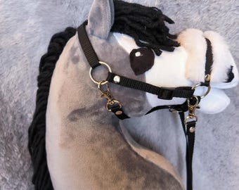 May include: A grey hobby horse head with a black mane and a black bridle. The horse features a white muzzle and black eye patches. The bridle has gold-coloured metal hardware and a black lead rope.