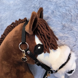 May include: A brown hobby horse head with a black bridle and reins. The horse has a white muzzle, brown mane, and ears. The background is a soft, gray, furry material.