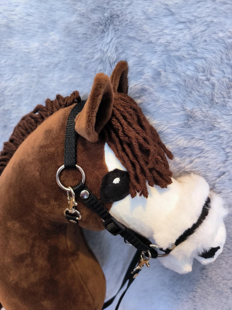 May include: A brown hobby horse head with a black bridle and reins. The horse has a white muzzle, brown mane, and ears. The background is a soft, gray, furry material.