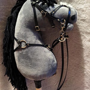 Könnte beinhalten: Ein graues Plüsch-Steckenpferd mit schwarzer Mähne und schwarzem Lederzaumzeug. Das Spielzeugpferd hat einen Holzstab als Griff und ist für Kinderspiele konzipiert.