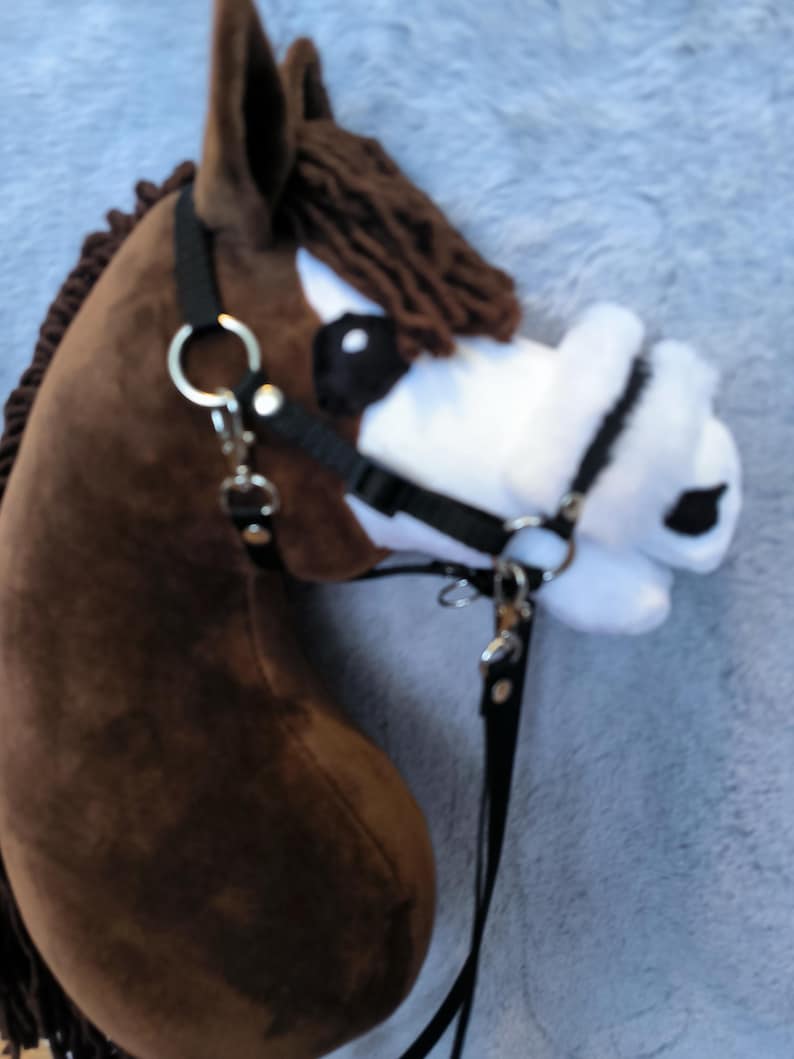May include: A brown hobby horse head with a black bridle and reins. The horse has a white muzzle with black spots and a brown mane. The toy is made of soft fabric and is designed for children.