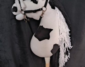 May include: A black and white spotted plush horse head with a black bridle and white mane and tail. The horse is attached to a wooden stick.