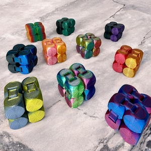 Könnte beinhalten: Eine Sammlung von bunten, mehrseitigen, geometrischen Würfeln mit einem regenbogenfarbenen, irisierenden Finish. Die Würfel sind aus Kunststoff und haben eine Vielzahl von Farben, darunter Rot, Orange, Gelb, Grün, Blau und Lila.