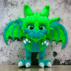 Puede incluir: Una figurita de dragón verde y azul con alas grandes. El dragón tiene una expresión amigable y ojos grandes.