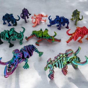 Puede incluir: Una colección de diez figuritas de mamut esqueléticas metálicas y coloridas. Cada figurita está hecha de un color diferente, incluyendo rojo, azul, verde, morado y naranja.