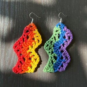 May include: A pair of rainbow crochet earrings with a wavy design. The earrings are made with different colors of yarn, including red, orange, yellow, green, blue, and purple.