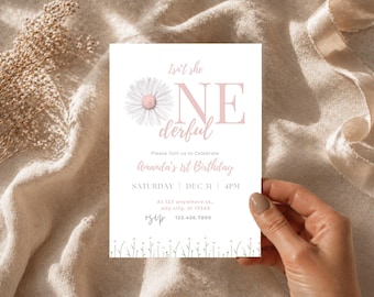 May include: A white invitation card with a daisy illustration and the text "Isn't she ONE derful" in pink. The card is for Amanda's 1st birthday, with the date and time listed. The card is held by a hand.
