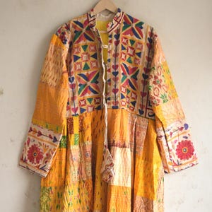 May include: A long-sleeved, knee-length coat featuring a patchwork design in shades of yellow, orange, and cream. The garment includes a mandarin collar, a front tie closure, and intricate embroidered floral and geometric patterns throughout.