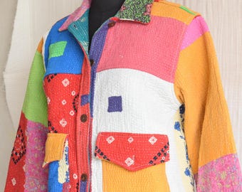 May include: A long-sleeve jacket constructed from multicolored patchwork fabric featuring various patterns including floral, geometric, and solid blocks in red, blue, yellow, pink, and white. The jacket has a collar, front buttons, and two pockets.