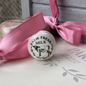 Puede incluir: Pomo de cer&aacute;mica blanco con una ilustraci&oacute;n en blanco y negro de una vaca y el texto "Farm Fresh Milk".