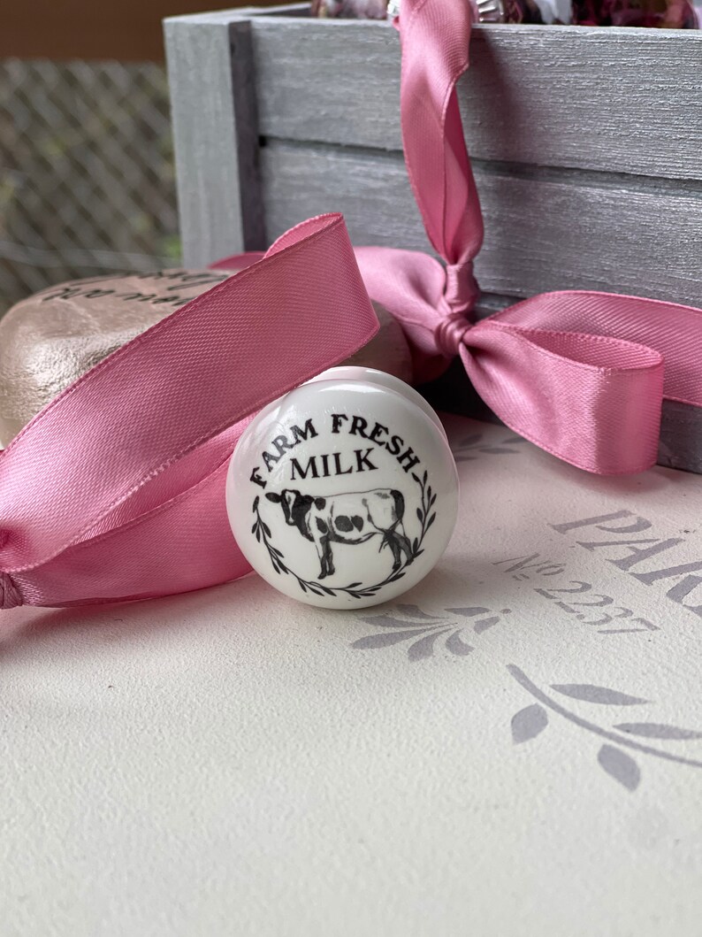 Puede incluir: Pomo de cer&aacute;mica blanco con una ilustraci&oacute;n en blanco y negro de una vaca y el texto "Farm Fresh Milk".