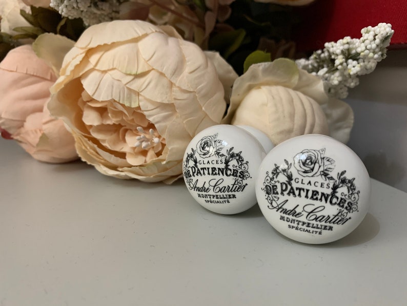 Puede incluir: Dos pomos de cer&aacute;mica blanca con letras negras que dicen "Glaces De Patiences Andre Cartier Montpellier Specialite".