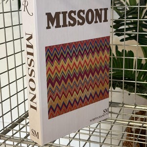 May include: A hardcover book titled "MISSONI" with a colorful zigzag pattern on the cover. The book is white with the brand name in large brown letters. The spine also features the brand name.