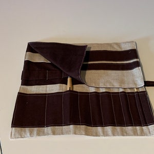 May include: A brown and beige fabric roll with multiple pockets for storing tools. The roll is tied with a brown fabric strap.