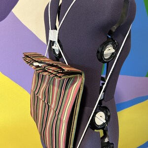 Puede incluir: Una bolsa de tela a rayas con una cuerda blanca atada a un maniquí. La bolsa está doblada y tiene un patrón de rayas negras, rosas, verdes y amarillas.