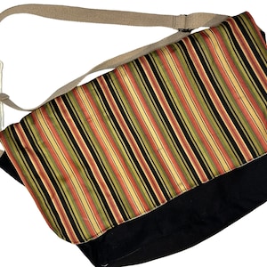May include: A black canvas messenger bag with a striped fabric flap. The flap has alternating stripes of black, yellow, red, and green.