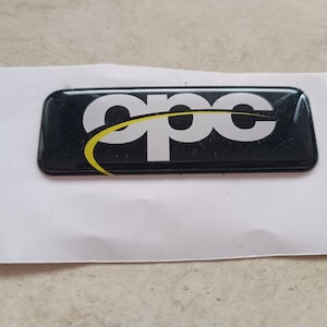 Puede incluir: Logotipo en blanco y negro con un arco amarillo, el logotipo dice "opc"
