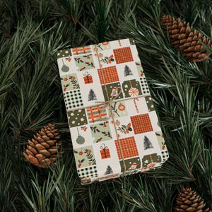 Könnte beinhalten: Ein Geschenk, das in festliches Papier mit einem Patchwork-Design verpackt ist. Das Papier zeigt Weihnachtsmotive wie Kugeln, Geschenke, Bäume und Zuckerstangen in Rot, Grün und Schwarz. Das Geschenk ist mit Bindfaden gebunden und liegt auf einem Bett aus Kiefernadeln und Tannenzapfen.