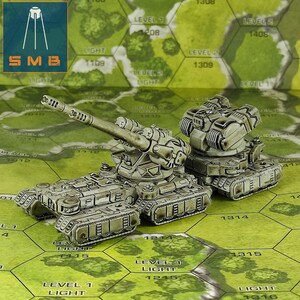 May include: Two detailed, miniature military tanks in shades of gray and green sit on a hexagonal game board. The tanks have intricate designs, including turrets and treads. The board features text like "LEVEL 1 LIGHT" and "SMB" in a corner.