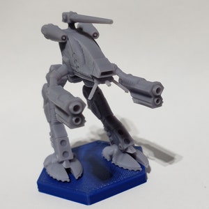 May include: A gray plastic model of a futuristic mech with three barrels on each arm and a single barrel on the top. The mech is standing on a blue hexagonal base.