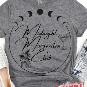 May include: Gray t-shirt with a black graphic design of a witch with a hat, a margarita glass, and the text "Midnight Margaritas Club" in a circle with crescent moons around it.