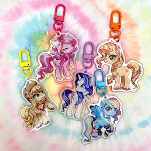 Puede incluir: Cinco llaveros de pony de dibujos animados coloridos con fondos de acrílico transparente. Cada llavero presenta un pony diferente con un diseño y una combinación de colores únicos. Los llaveros están unidos a anillos de metal plateado.