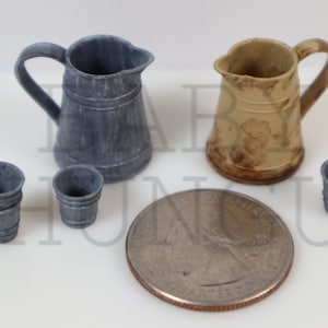 May include: A miniature kitchenware set, featuring two pitchers and four cups. The pitchers are ceramic and have a rustic, aged appearance. One pitcher is grey and the other is beige. The cups are stacked and also made of ceramic. The set is displayed on a white surface with a US quarter for scale.