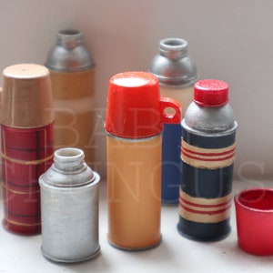 May include: A collection of six vintage-style thermoses in various colors and patterns, including red, orange, blue, and plaid. The thermoses are made of metal and have a classic design.