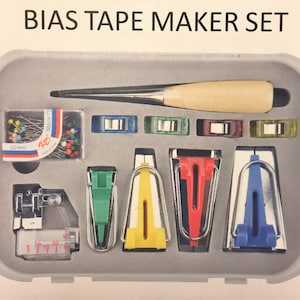May include: A gray plastic case with a set of bias tape makers. The case includes a variety of sizes and colors of bias tape makers, as well as a needle threader, a ruler, and a pack of pins. The case also includes a wooden tool for pressing the bias tape.