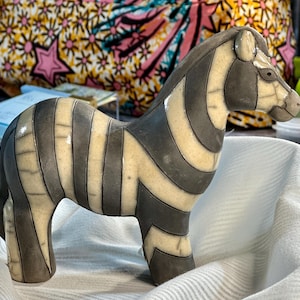May include: A ceramic zebra figurine with black and white stripes. The figurine is standing on a white fabric surface.