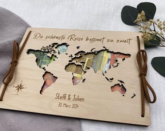 Könnte beinhalten: Eine Holz-Weltkarte mit ausgeschnittenen Kontinenten, gefüllt mit bunten Währungen. Die Karte ist mit Namen und einem Datum personalisiert und mit braunen Lederschnüren gebunden. Der Text lautet "Die schönste Reise beginnt zu zweit."