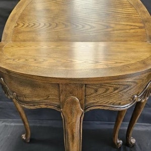 May include: A wooden table with a curved top and three legs. The table is made of a light brown wood with a natural finish. The table has a curved top and three legs. The legs are carved with a decorative design.