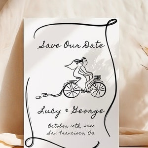 Könnte beinhalten: Eine schwarz-weiße Save-the-Date-Karte mit einer handgezeichneten Illustration eines Paares auf einem Fahrrad. Der Text lautet "Save Our Date", "Lucy & George", "October 15th, 2025" und "San Francisco, Ca."