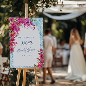 May include: A white sign with blue and pink watercolor floral designs. The sign says "Welcome to Lucy's Bridal Shower 25 May 2025".