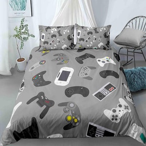 Könnte beinhalten: Ein grauer Bettbezug mit einem Muster aus verschiedenen Videospielcontrollern in Schwarz, Weiß und Grau. Der Bettbezug liegt auf einem Bett mit zwei passenden Kissenbezügen.