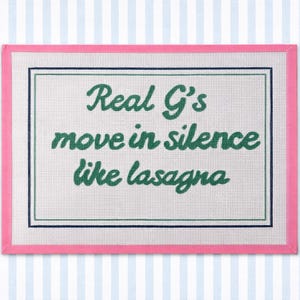 May include: A rectangular, white, textured surface with the text "Real G's move in silence like lasagna" in green script. The text is framed by a dark green and pink border, set against a blue and white striped background.